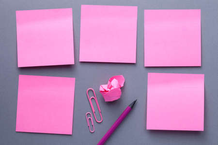 Pink sticky note paper with office supplies on grey paper background. Office flat lay composition with paper clip, crumbled paper and pencil. Copy space. Top viewの写真素材