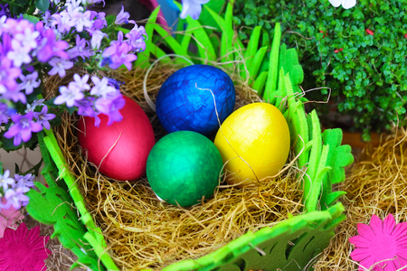 Four colorful easter eggs in a natural straw with flowers, close up