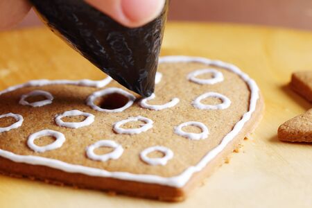 Woman decorating gingerbread cookies. Close up view with selective focus.