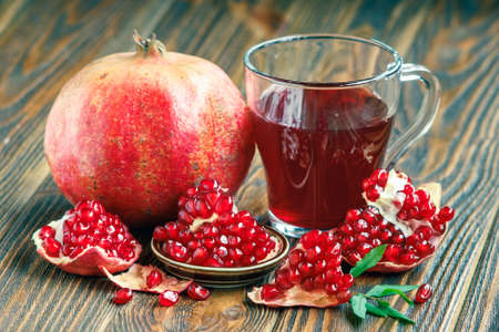 glass of pomegranate juice with ripe fresh punica granatum fruits with leaves on wooden table close-upの写真素材