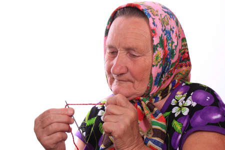The elderly woman inserting the red thread in the needleの写真素材