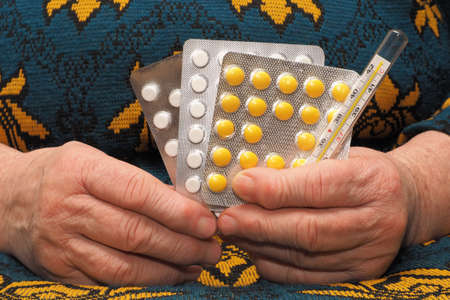 Medicines and the thermometer in hands of the elderly womanの写真素材