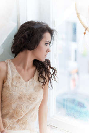 Beautiful young brunette woman looking out the window, natural lightの写真素材