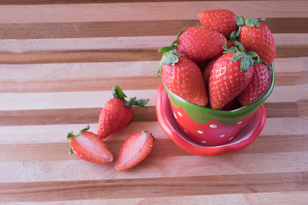 Fresh red whole and half cut strawberry in strawberry pot on red brown wooden tableFresh strawberry in strawberry cupの写真素材
