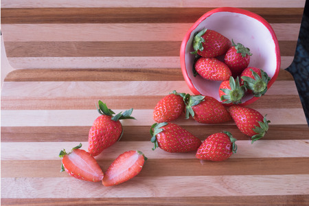 Fresh red whole and half cut strawberry in strawberry pot spill and scatter on red brown wooden tableFresh strawberry in strawberry cupの写真素材