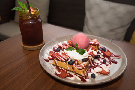Fresh strawberry blueberry waffle with strawberry ice cream and ice strawberry tea on wooden table...
