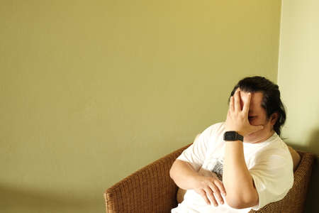 Long hair stress man sitting in chair hold head with hand in living room with yellow wall background in the houseの写真素材
