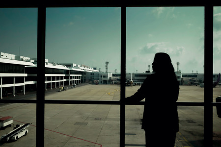 Woman is waiting the flight and looking out of airport window before walking to the gate at take off/Woman is waiting the flight at airport airportの写真素材