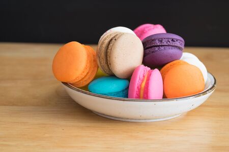colorful macaroon in white ceramic plate with all flavors on wooden table/colorful macaroon in ceramic plateの写真素材