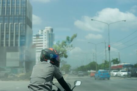 man biker with helmet and jacket riding a motorcycle on road in city waiting for traffic light to go in daytimeの写真素材
