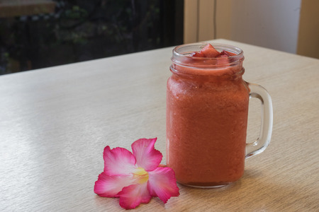 ice strawberry frappe juice on wooden table with pink fresh flower as healthy sweet food and drinkの写真素材