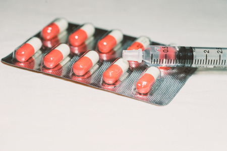 pill and medicine in many color and many tablet with needle and syringe on white table for cure and treatmentの写真素材