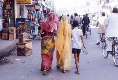 walking indian women in sari with kids along shops in indian town streetのeditorial素材