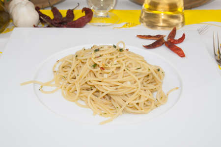 garlic hot pepper spaghetti side view close-up on white dish with hot pepper garnish and white wine glass and bottle, garlic and extra virgin olive oil on blured background, traditional italian foodの写真素材