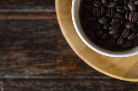 Top view of coffee beans in a cup on wooden background. For insert text design in advertising.の写真素材