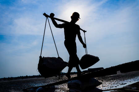 Silhouette of a man working on salt field in Thailand. A man workers transporting salt from the field.の写真素材