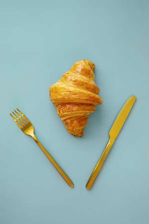 Single fresh croissant on a blue background viewed from above. Top view