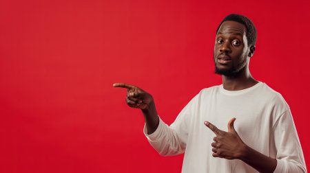 Young african american man pointing at copy space on red backgroundの素材