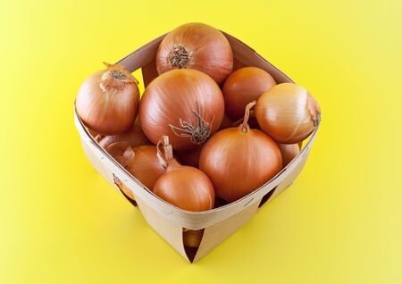 Onions in box on yellow background.の写真素材