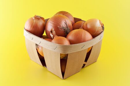 Onions in a box on yellow background.の写真素材