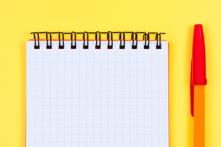Notepad and ballpen on yellow background.