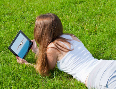 Woman looks pictures wildlife on tablet lying on grass.の写真素材