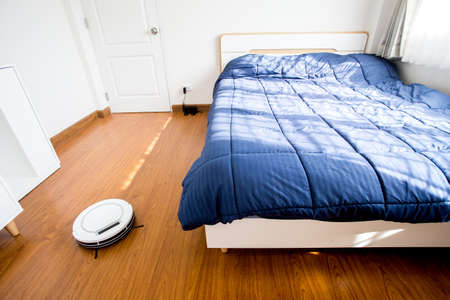 Robotic vacuum cleaner on laminate wood floor in bedroom.の写真素材