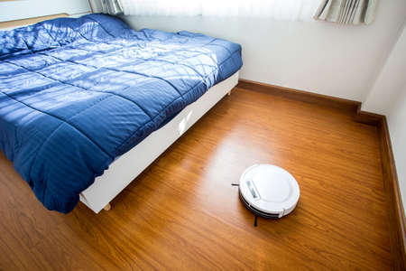 Robotic vacuum cleaner on laminate wood floor of bedroom.の写真素材