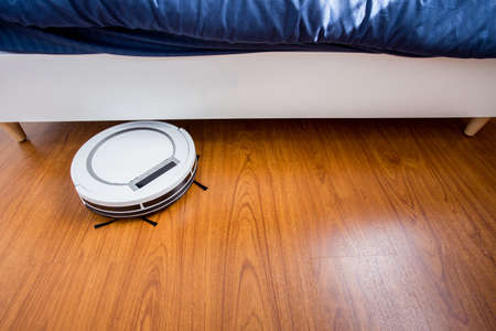 Robotic vacuum cleaner on laminate wood floor of bedroom.の写真素材