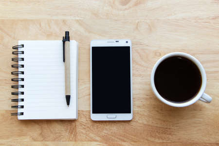 Notepad, smartphone and black coffee on wood table.の写真素材
