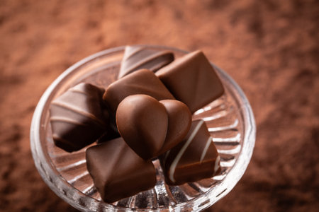 Chocolate candies in a glass bowl on a brown background.