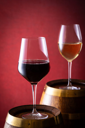 Two glasses of red and white wine on a wooden barrel on a red background