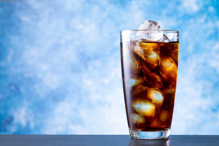 Cola with ice cubes in glass on blue background. Close up.