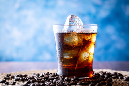 Cola with ice cubes and coffee beans on a blue background. Selective focus.