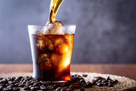 Cola with ice cubes and coffee beans on a dark background. Selective focus.