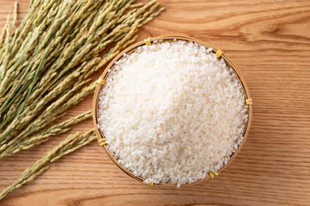 Bowl with rice grains and spikelets on wooden table, top view