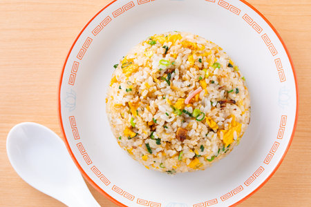 Fried rice with vegetables in a white plate on a wooden tableの写真素材