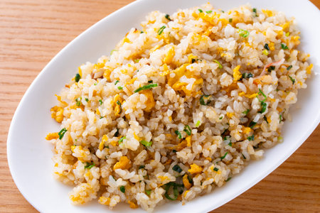 Fried rice with egg and herbs in white plate on wooden tableの写真素材