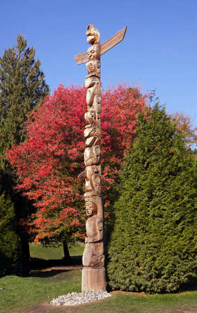 Totem pole in fall in front of red maple treeの写真素材
