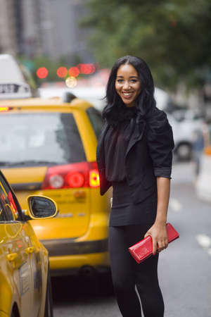 Smiling African-American woman on city street, amidst taxi cabs, with blurred background