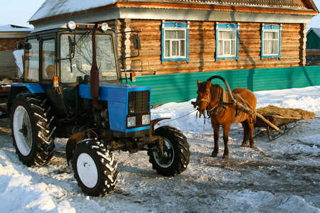 A sleigh with a horse next to a blue tractor.