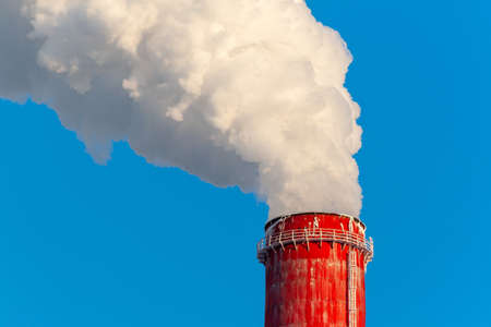 Pipes of thermal power plants on a frosty winter day, close-up. White thick smoke from high pipes of a thermal power plant. White steam on a blue sky on a frosty winter day.の写真素材
