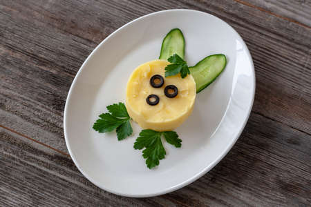 Vegetarian dish: Mashed potatoes with fresh cucumbers and greens, made in the shape of a bunny, on a...