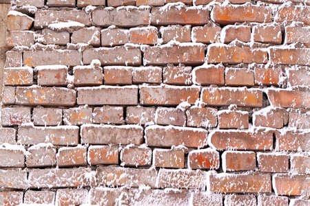 The texture of an old brick wall covered with snow. Uneven brickwork.