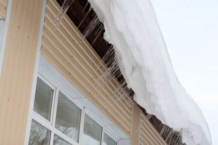 The snow and large icicles hanging dangerously from the edge of the roof. Scene snowy winter in...