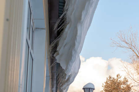 The snow and large icicles hanging dangerously from the edge of the roof. Scene snowy winter in Siberia.の写真素材
