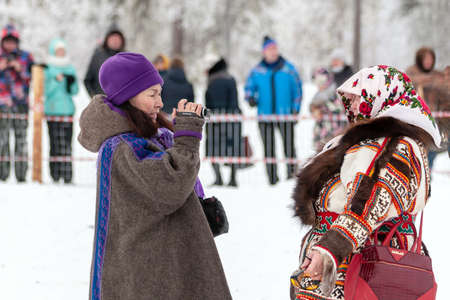 Russkinskaya, Surgut, Russia, 03/23/2019: open traditional holiday of the peoples of Siberia. Feast of reindeer herders. Woman tourist shoots a local woman in traditional clothes on video.のeditorial素材