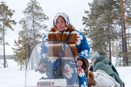 Russkinskaya, Surgut, Russia, 03/23/2019: open traditional holiday of reindeer herders and fishermen, indigenous peoples of Siberia. A local woman in a national costume drives a snowmobile.のeditorial素材