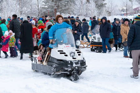 Russkinskaya, Surgut, Russia, 03/23/2019: open traditional holiday of reindeer herders and fishermen, indigenous peoples of Siberia. Aborigines-Khanty ride children on a snowmobiles.のeditorial素材