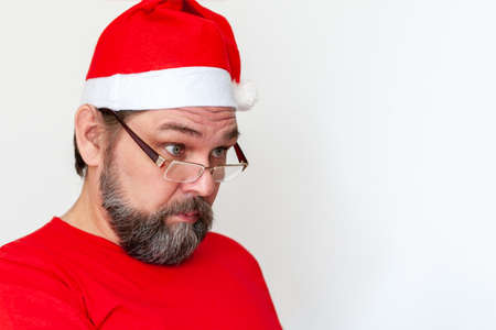 Surprised Santa Claus with a dark beard. A man with a beard, glasses and a red Santa hat on a light background with copy space.の写真素材